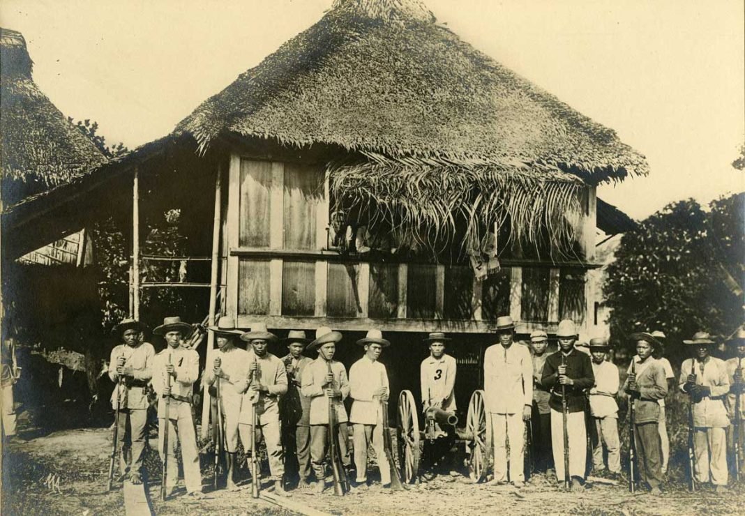 Jefes tagalos frente a una vivienda tradicional filipina o bahay en Baler (h. 1898-1899).